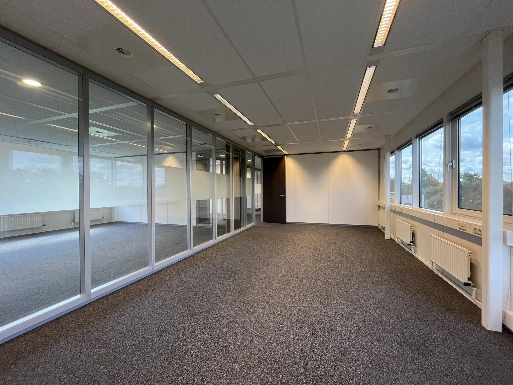 Leeg kantoor met glazen scheidingswand aan de Baarnsche Dijk, voorzien van grote ramen en systeemplafond.